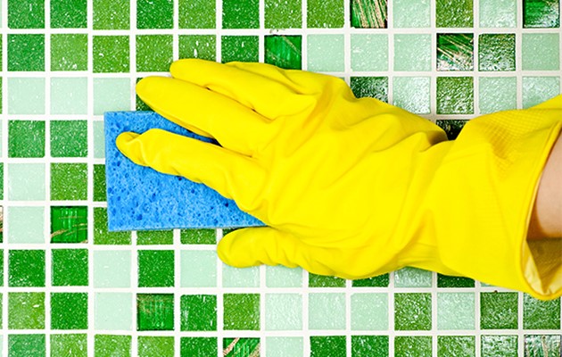 Gelber Handschuh mit Schwamm reinigt grüne Fliesen; Thema: putzen, reinigung.